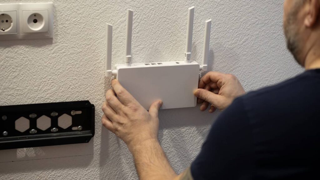 a man mounting a white wi fi router on a white wall next to a tv mount.jpg