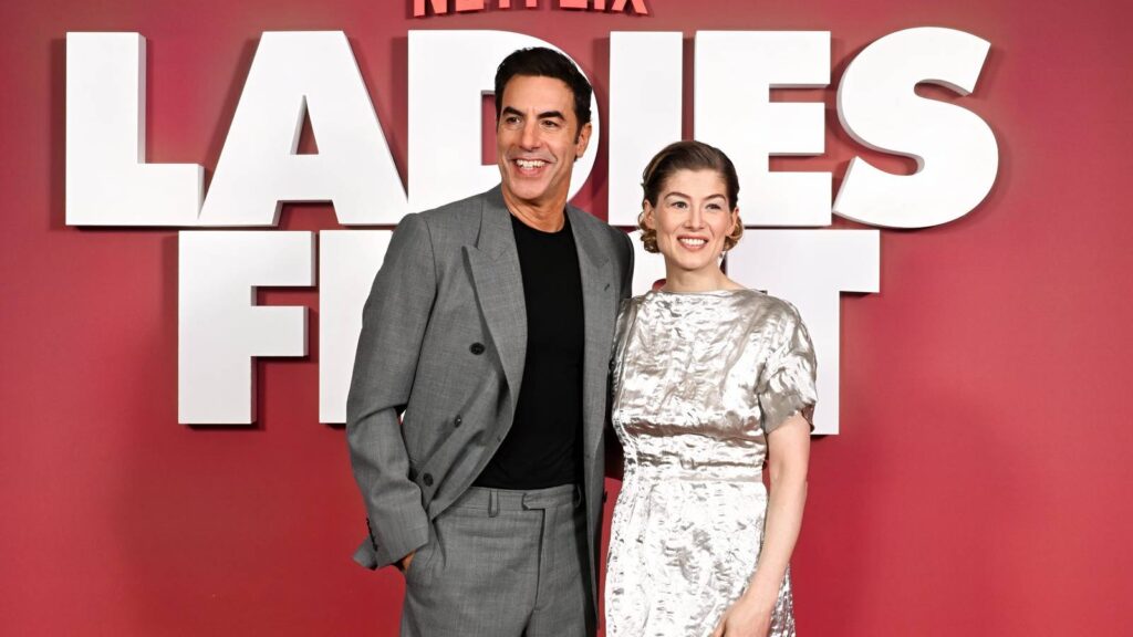 Women First director knew Sacha Baron Cohen and Rosamund Pike would thrive after only one Zoom name sacha baron cohen and rosamund pike stand next to each other on ladies first red carpet 1.jpg